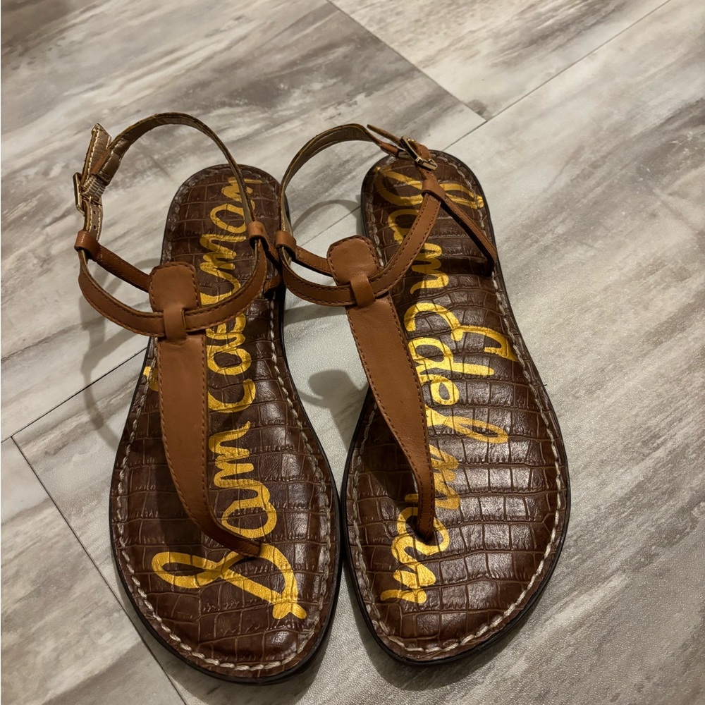 Brown flat thong-style sandals with ankle strap and gold lettering